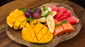 A wooden plate with sliced mango, watermelon, bananas, grapes, and lime on a wooden table.