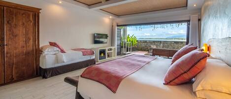 A bedroom with a large bed, wooden wardrobe, ceiling fan, and a view of the outdoors.