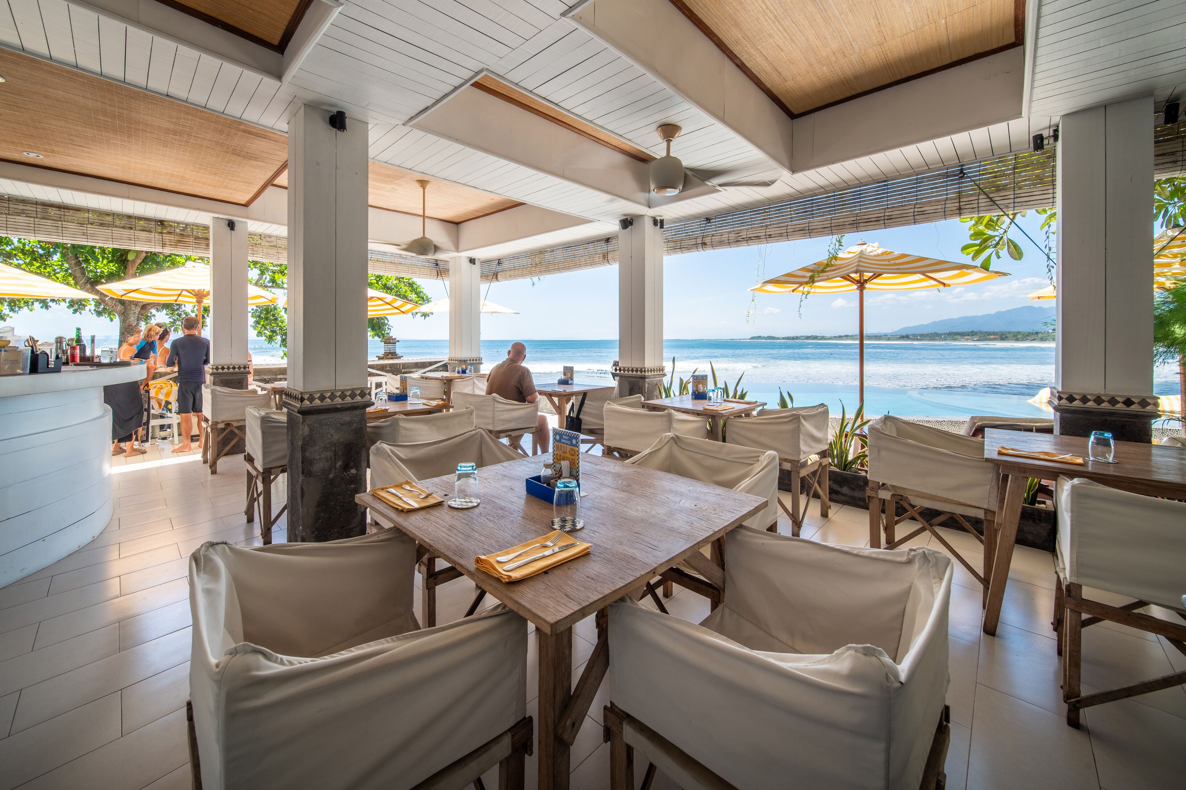 An outdoor dining area with tables and chairs, umbrellas, and a view of the sea.