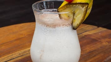 A cocktail in a glass with a cherry and a slice of lime on the rim.