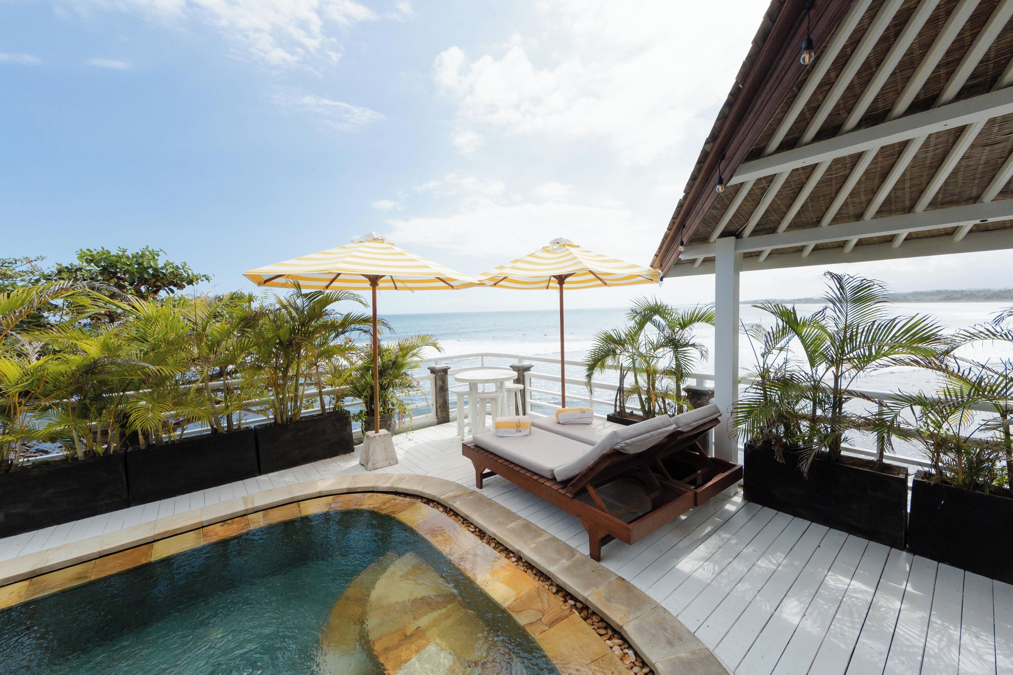 A pool area with lounge chairs and umbrellas, overlooking a beach.