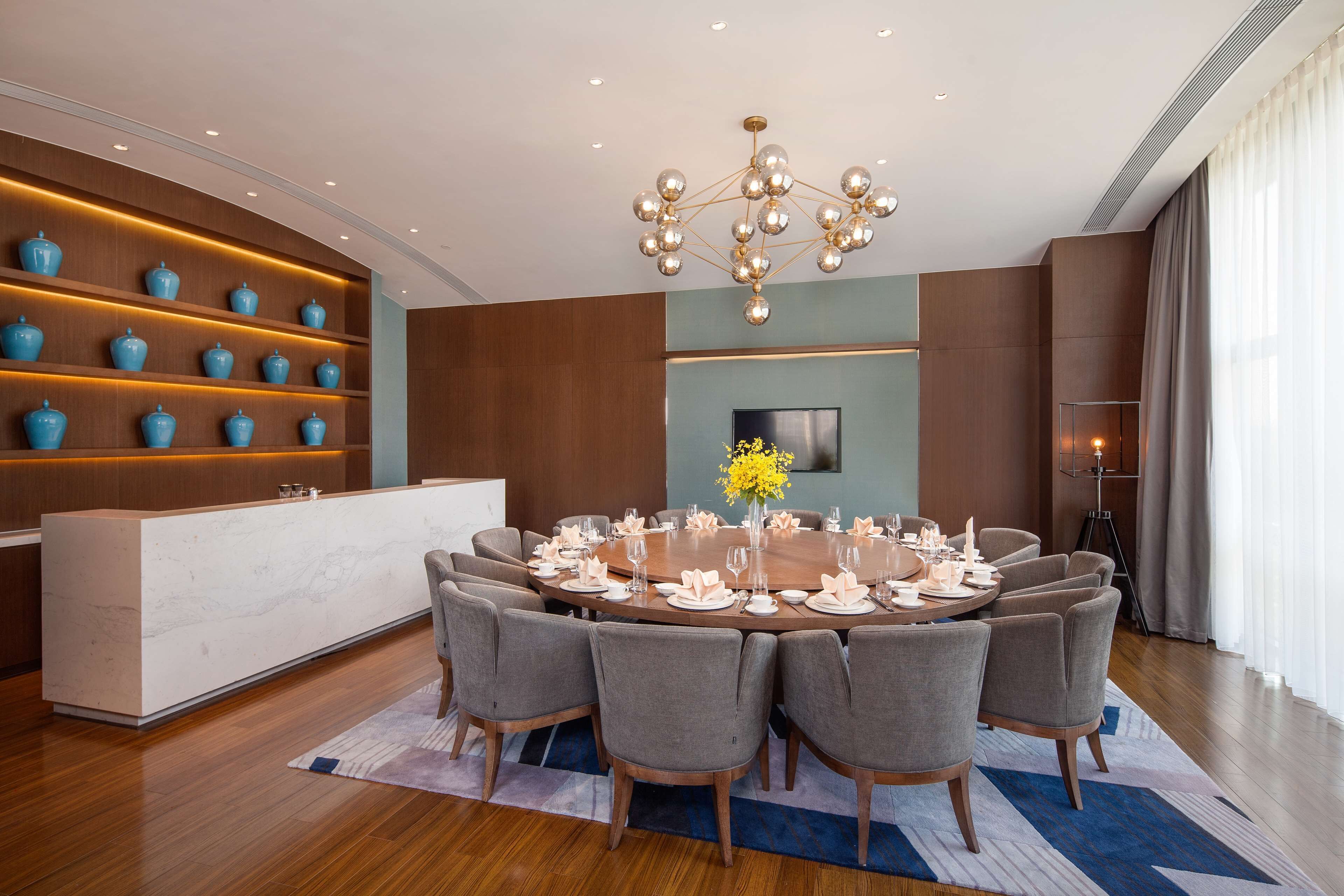 A modern dining area with a round table set for six, surrounded by grey upholstered chairs.