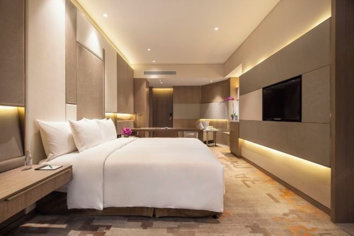 Una habitación de hotel moderna con una cama grande, mesitas de noche, un televisor de pantalla plana y una pequeña zona de escritorio.