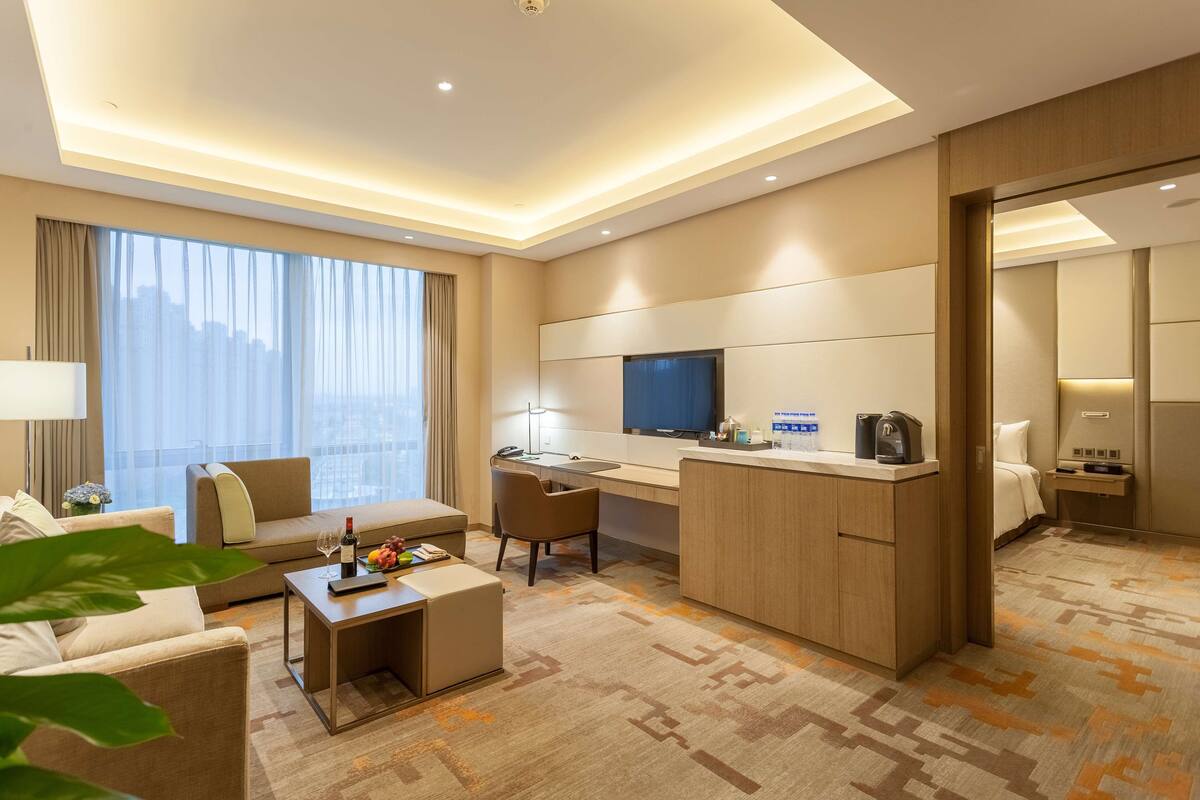 A modern hotel room with a sofa, a desk, a television, and a minibar.