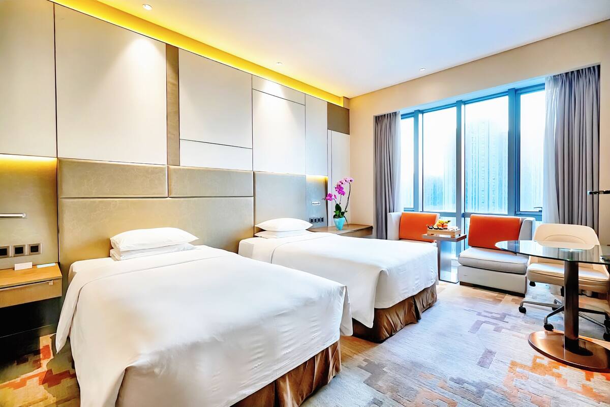 A hotel room with two beds, a sofa, a small table, and a view of the city.