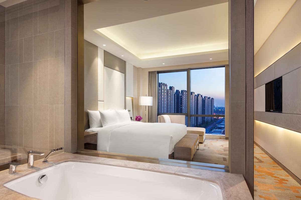 A modern hotel room with a large bed, a bathtub, and a city view.