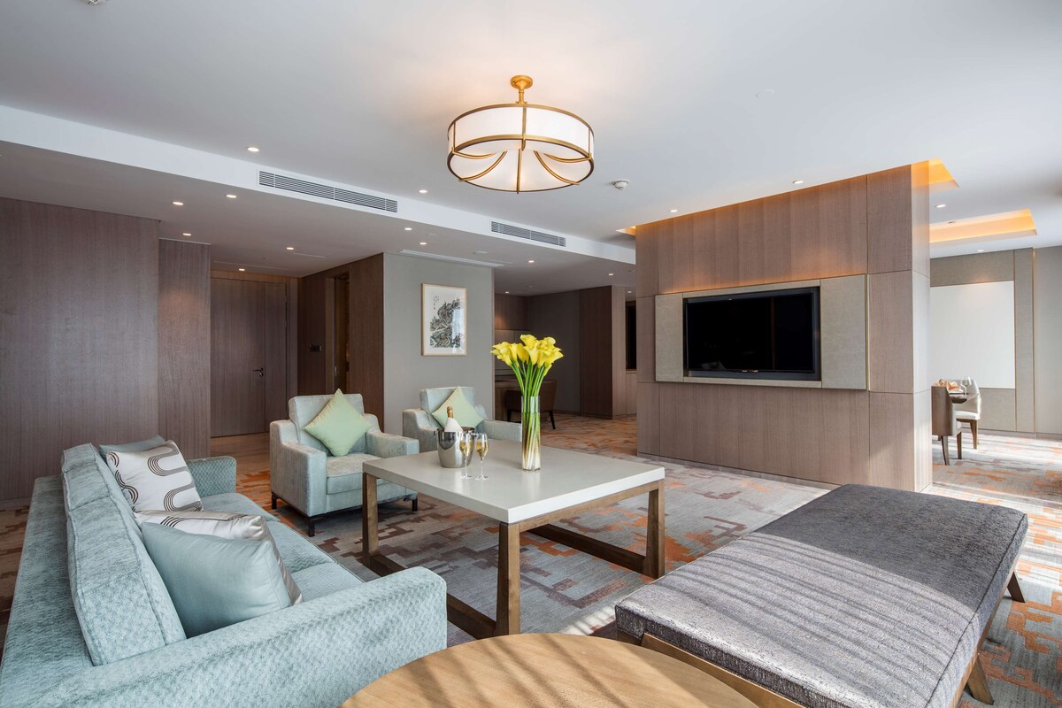 A modern living room with a sofa, armchairs, a coffee table, and a TV mounted on the wall.