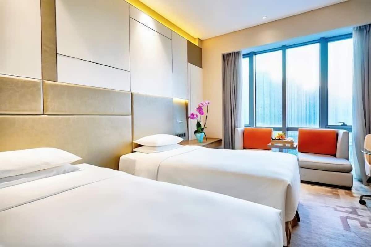 A hotel room with two beds, a sofa, a small table, and a large window with curtains.