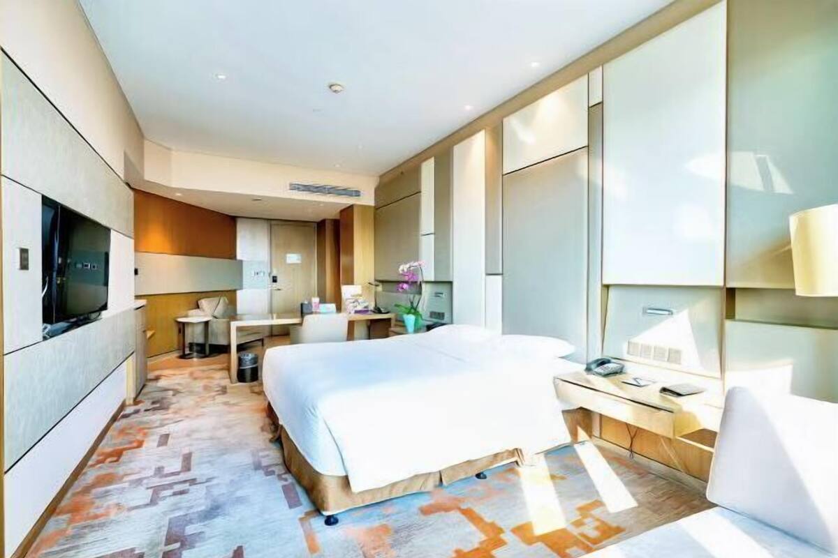 A modern hotel room with a bed, desk, chair, and television.