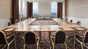 A conference room with a long table, chairs, and a view of a cityscape through large windows. - Apart Hotel Zurich Airport (Opfikon)