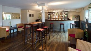 A bar area with stools, a counter, and a bar stocked with bottles. - Apart Hotel Zurich Airport (Opfikon)