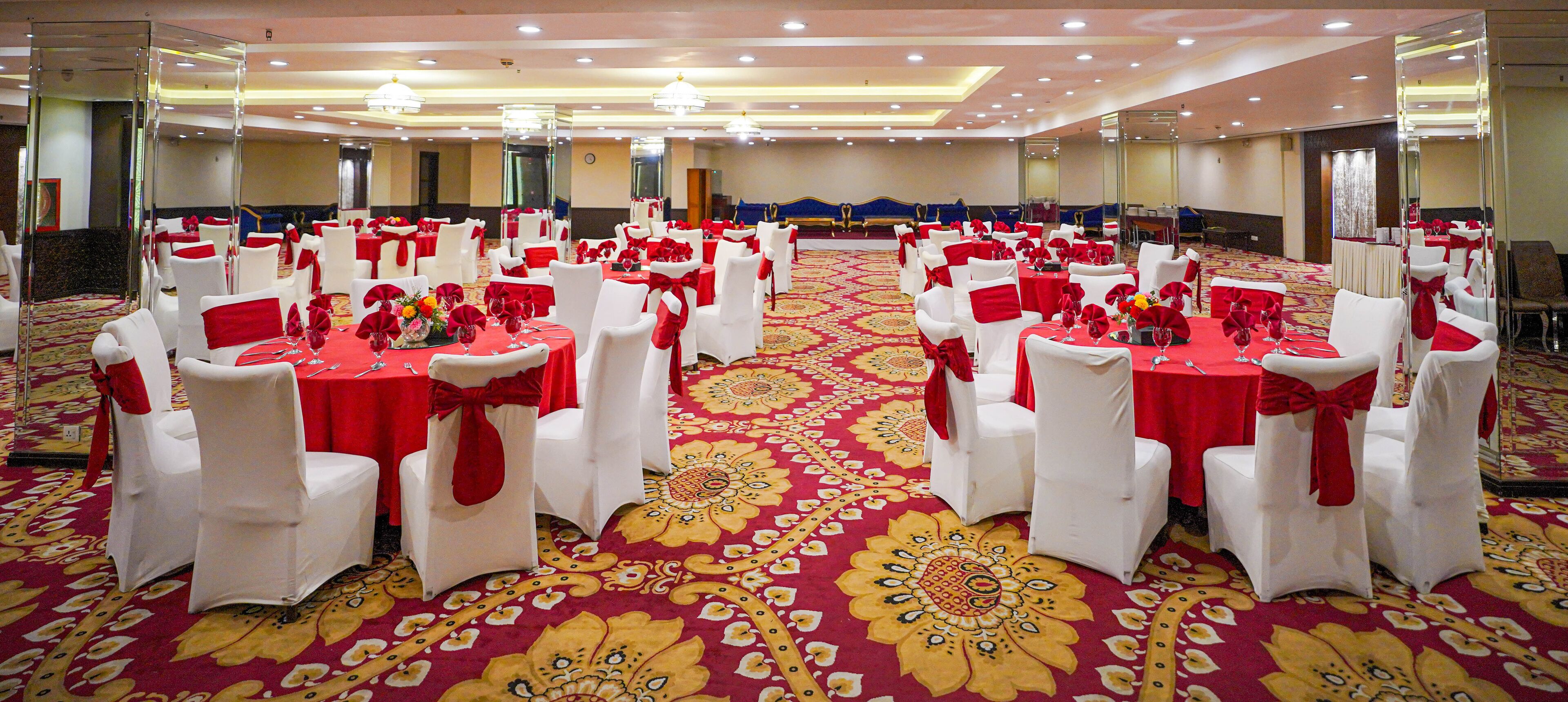 Una sala de banquets amb taules rodones, cadires blanques i estovalls vermells.
