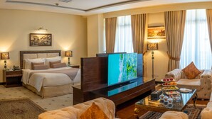 A hotel room with a bed, a TV, a sofa, and a coffee table with fruit. - Ramada by Wyndham Islamabad (Islamabad)