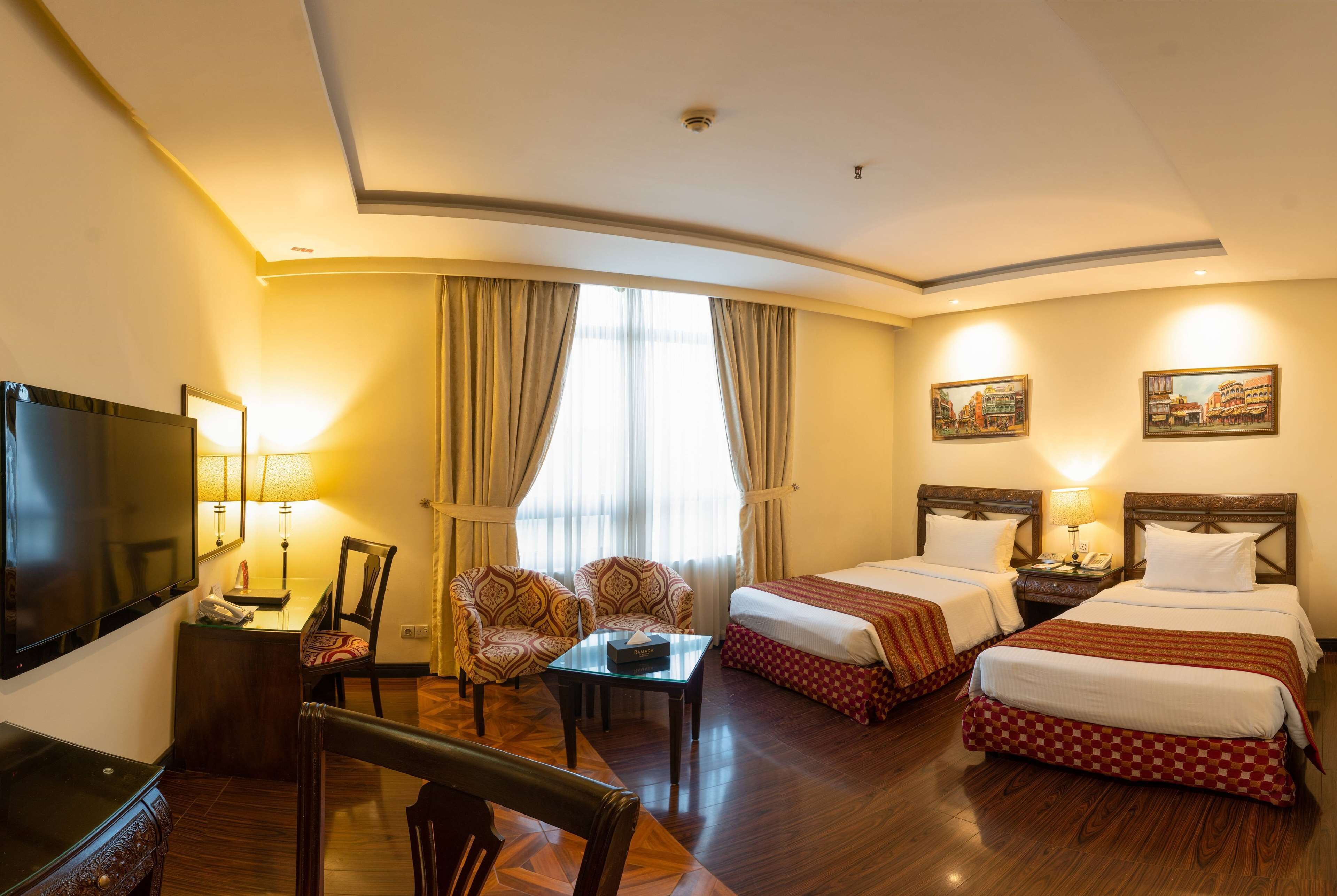 Habitación de hotel con dos camas, un escritorio con silla, televisión y ventana con cortinas.