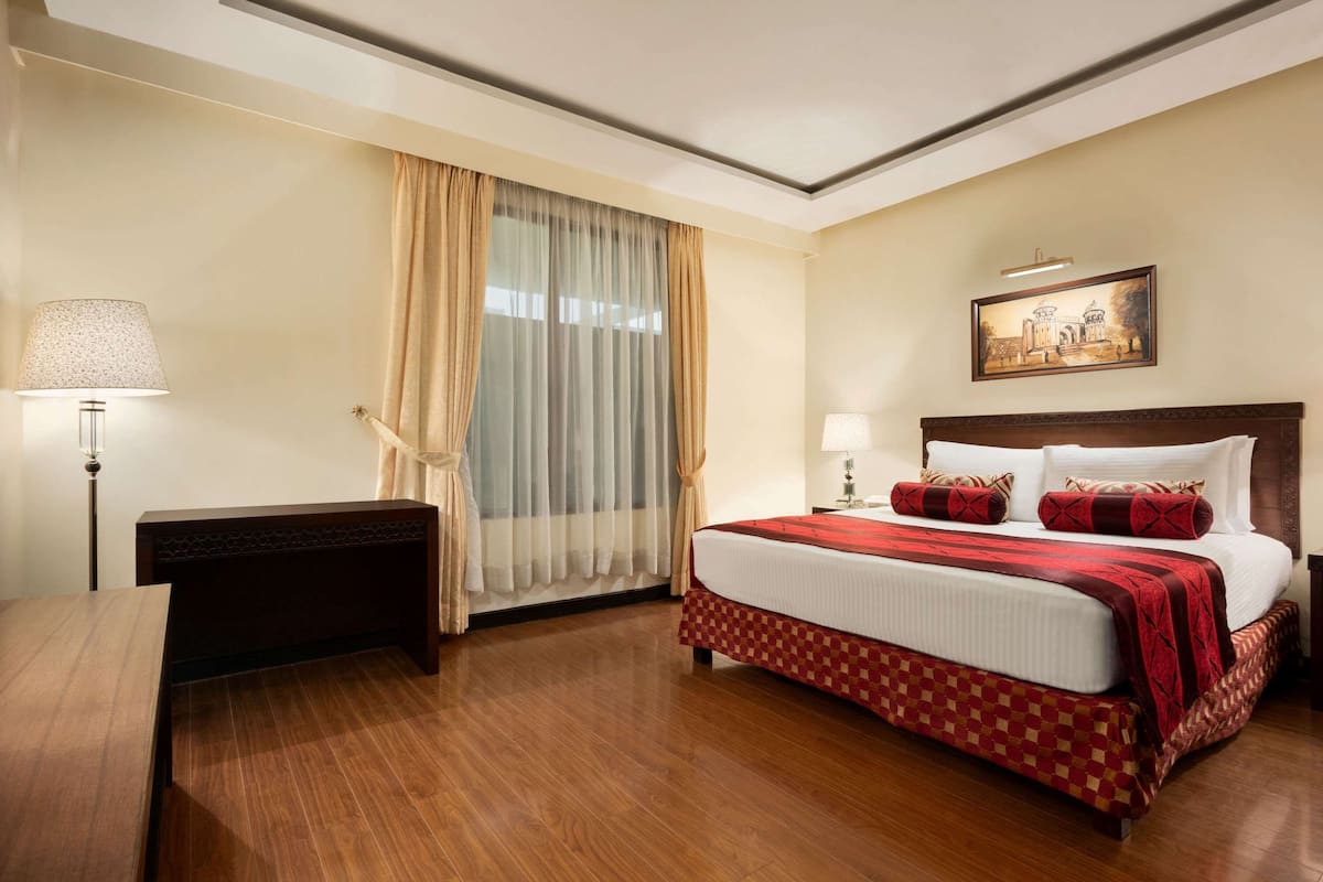 Una habitación de hotel con una cama grande, un escritorio, una lámpara y un cuadro en la pared.