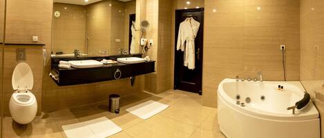 A modern bathroom with a large bathtub, a separate toilet, a vanity with a mirror, and a robe hanging on the wall.