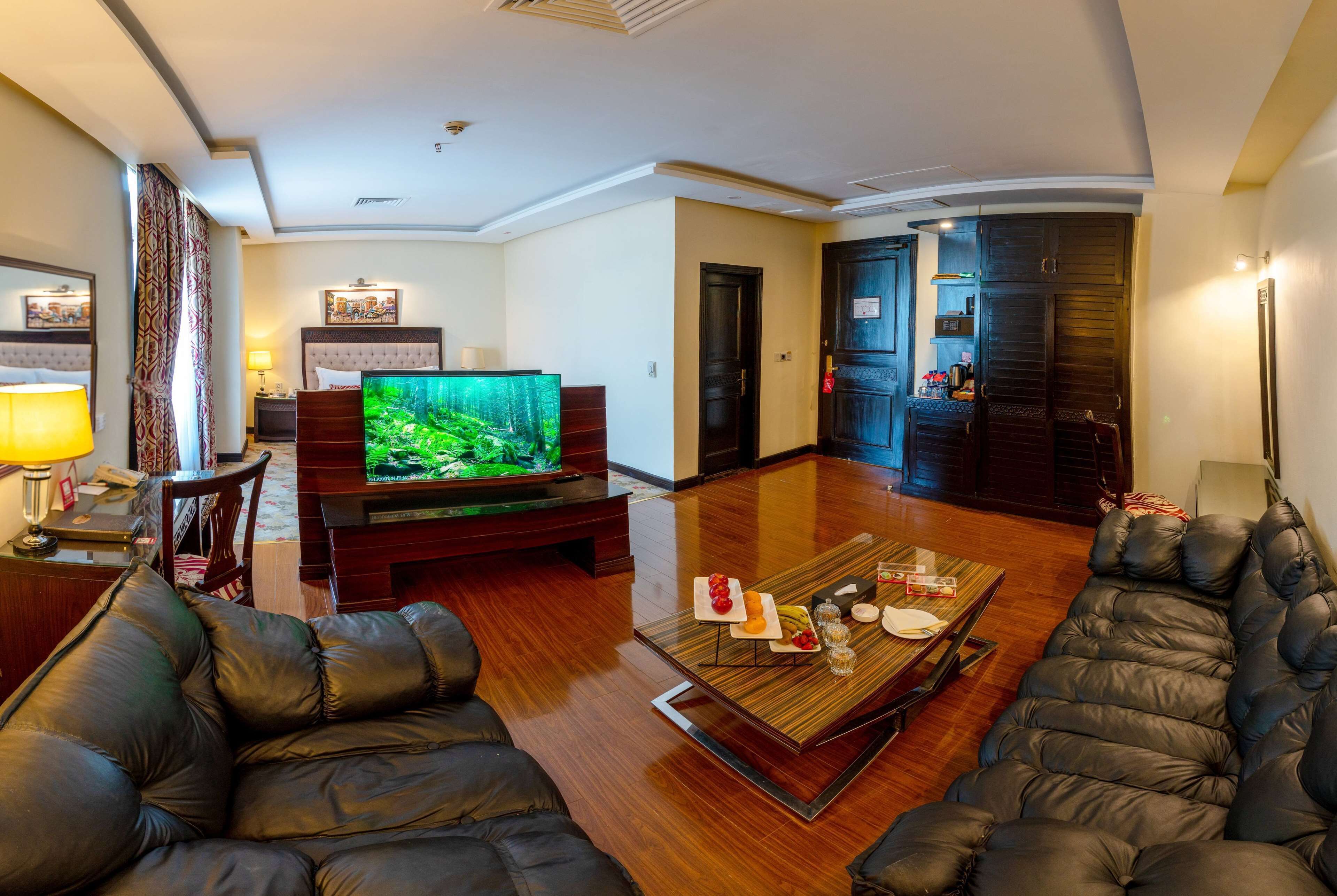 Een moderne woonkamer met een grote flatscreen-tv, leren banken, een houten salontafel en een donkerhouten garderobe.