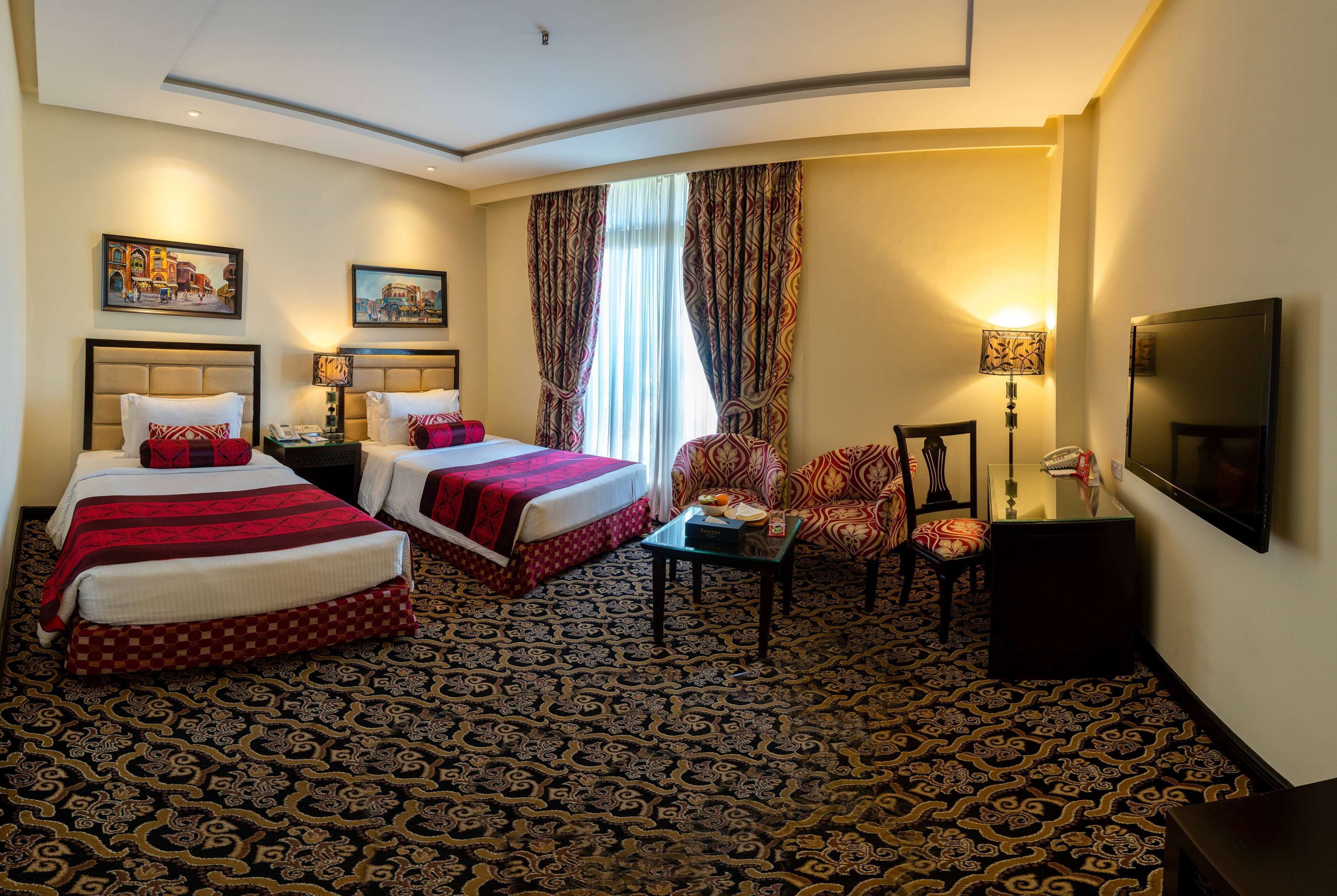 Habitación de hotel con dos camas, televisión, una silla y una mesita.