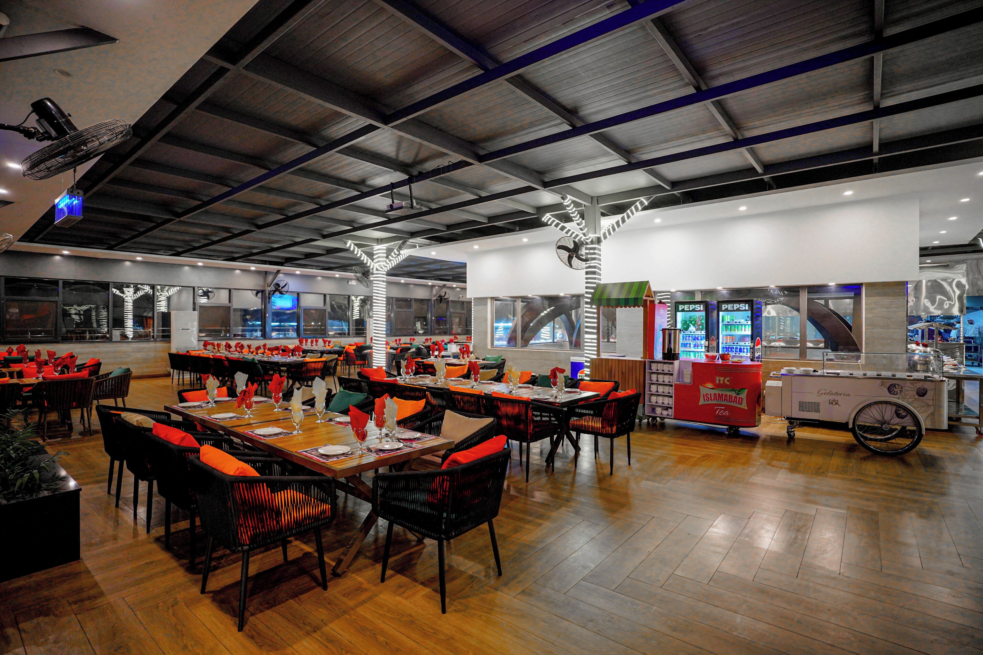 Un restaurante espacioso con techos altos y decoración moderna, que cuenta con varias mesas y sillas, además de un carrito de comida.