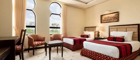A hotel room with two beds, a desk, a chair, and a piano.