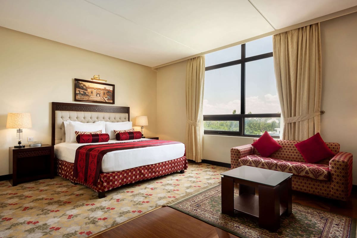 Una habitación de hotel con cama, sofá, una mesa de centro y un ventanal con cortinas.