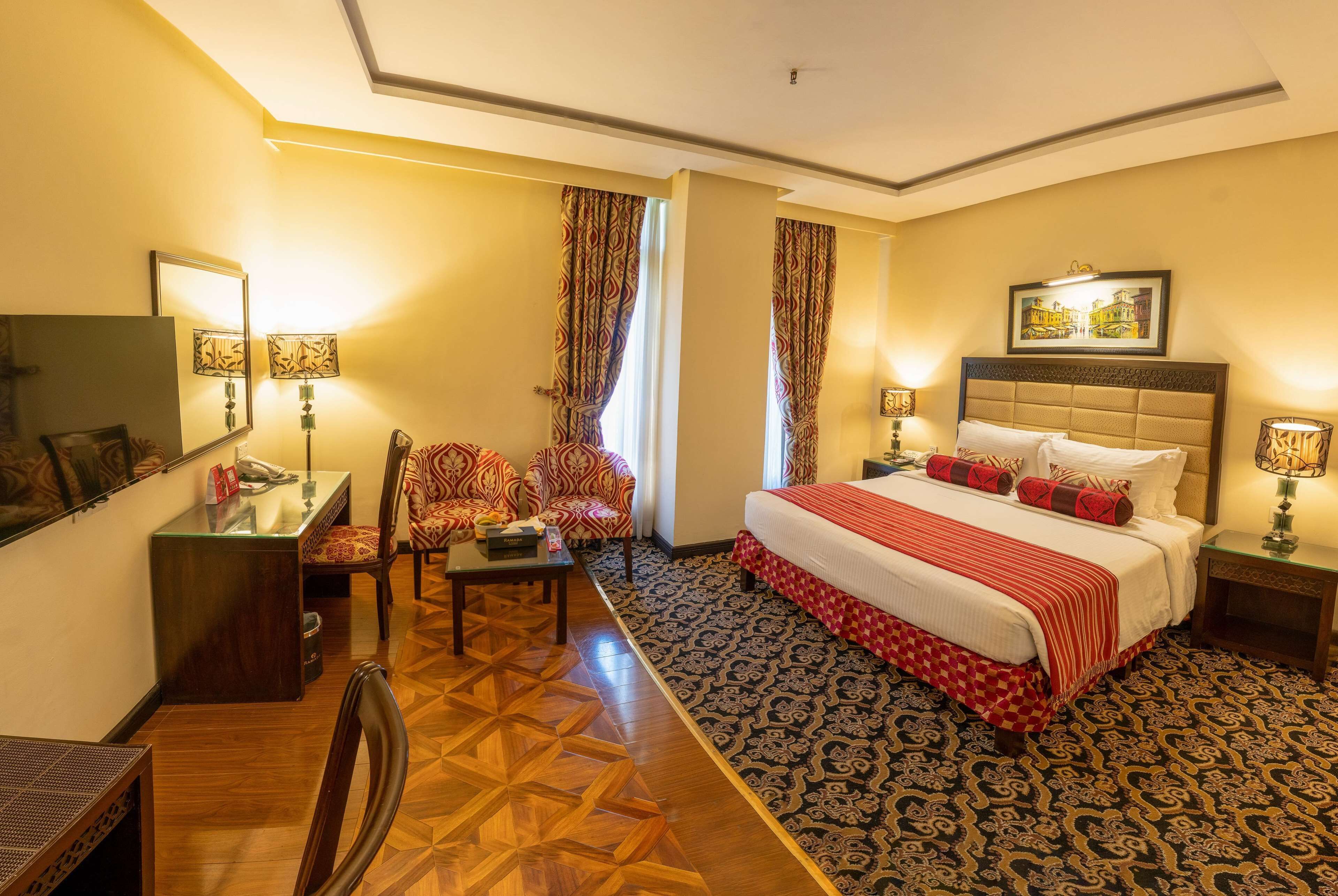 A hotel room with a bed, two chairs, a desk, and a mirror.