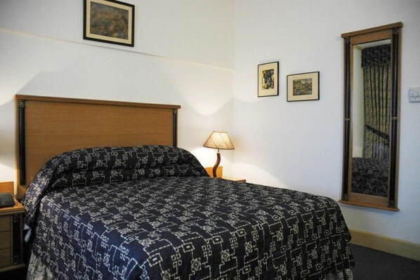 A neatly made bed with a patterned bedspread, a bedside lamp, and two framed pictures on the wall. - Hotel Mehran (Karachi)