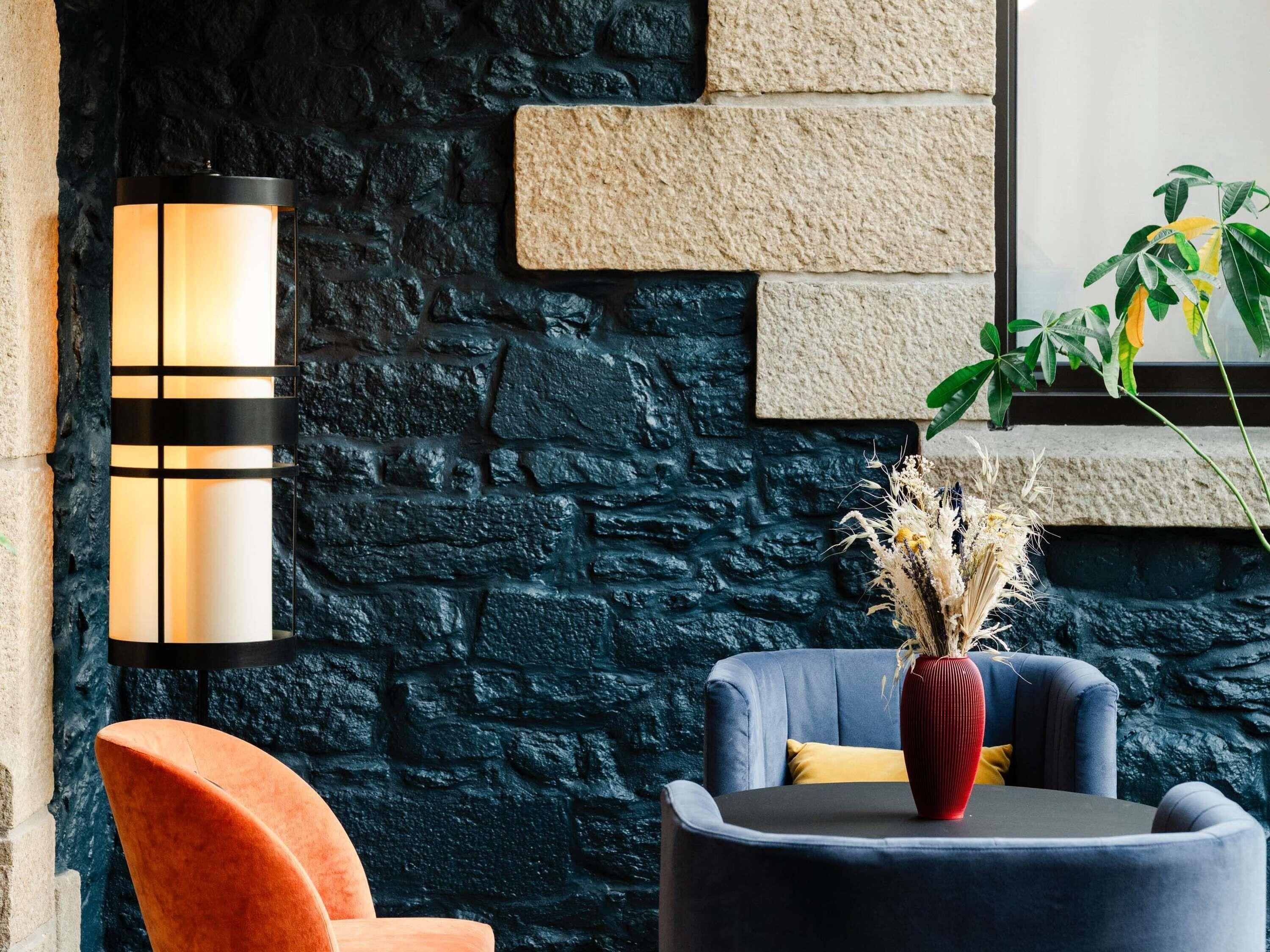 A modern interior with a stone wall, a round table with a vase, a blue chair, and a red chair.