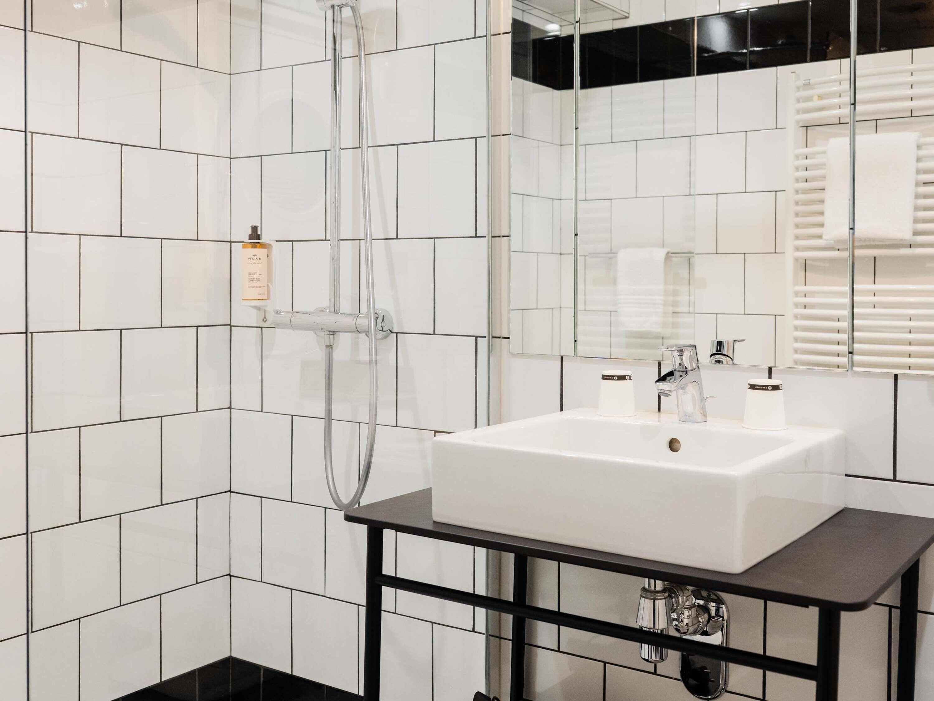 Un baño moderno con azulejos blancos, un lavabo blanco, un espejo y una ducha.