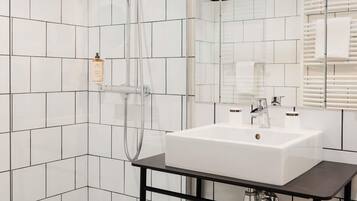 A modern bathroom with white tiles, a white sink, a mirror, and a shower.