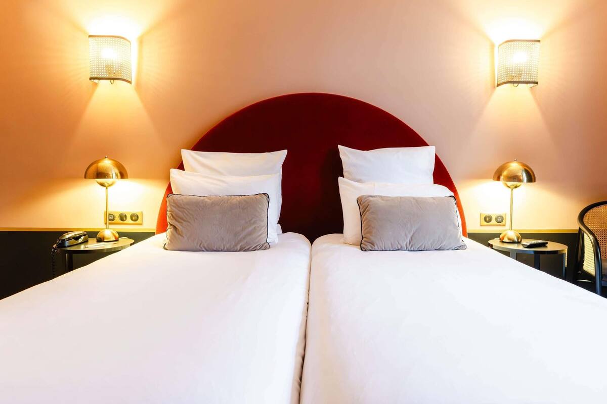 Een tweepersoonsbed met twee nachtkastjes, elk met een lamp, in een kamer met een rode hoofdbord en wandlampen.
