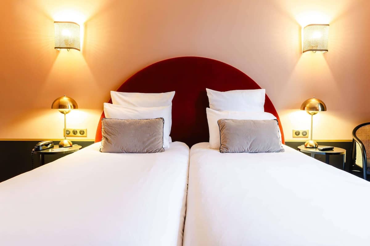A double bed with two bedside tables, each with a lamp, in a room with a red headboard and wall sconces.
