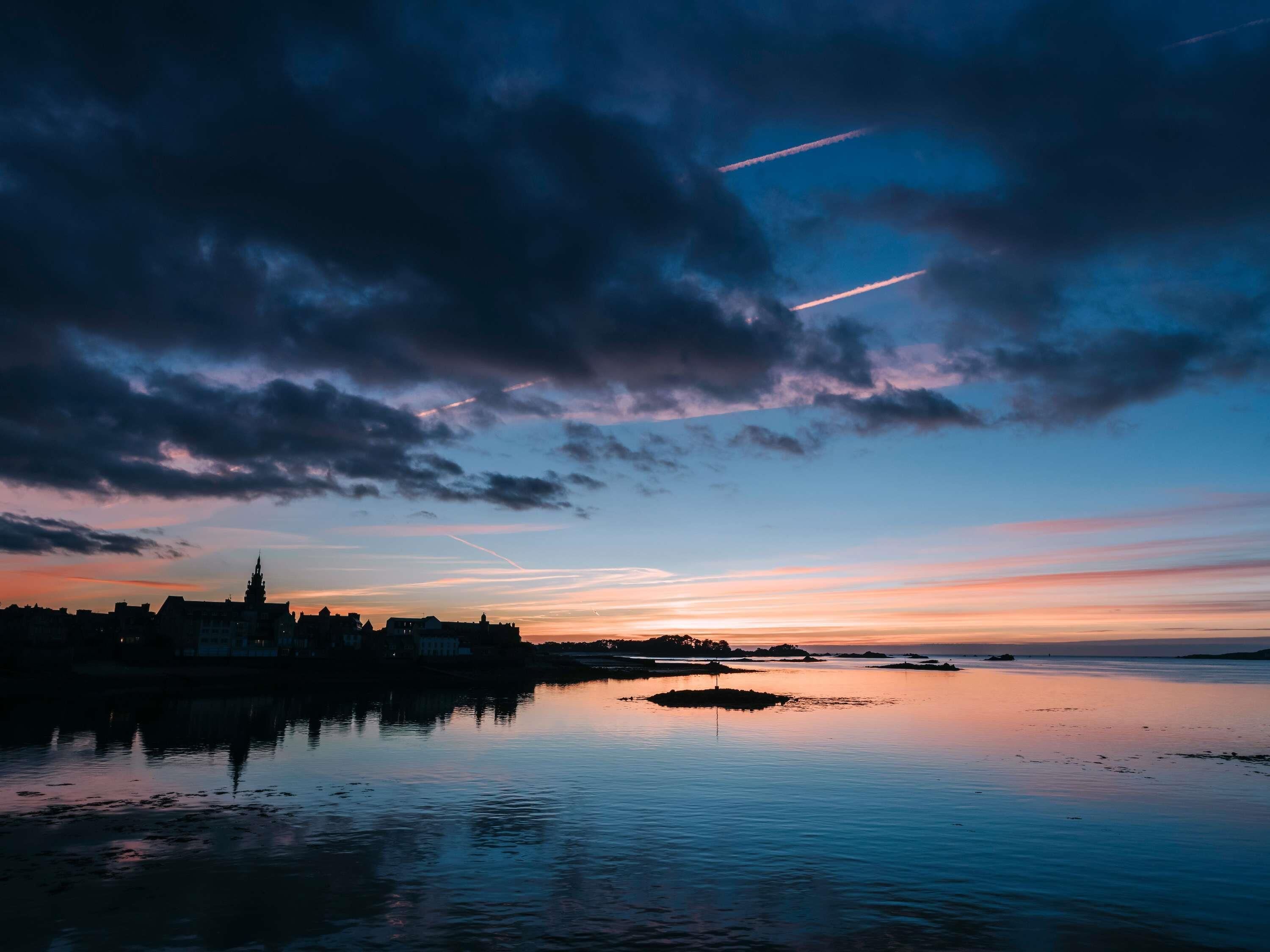 A calm waterfront at sunset with a silhouette of buildings and a church spire.