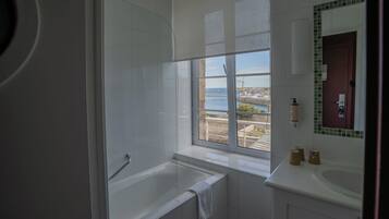 A modern bathroom with a bathtub, a shower, and a window with a view of a bridge and water body.