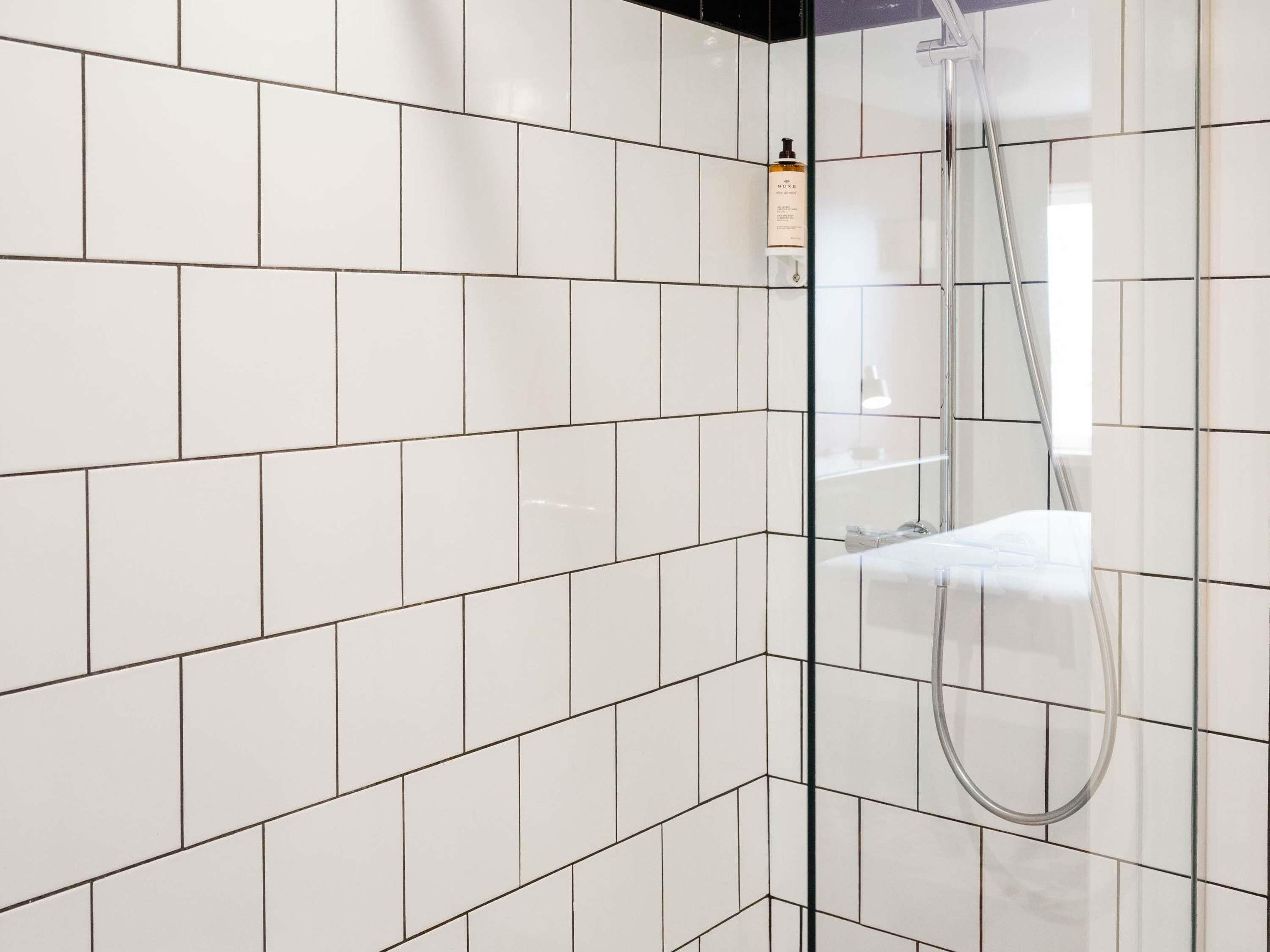 A modern shower area with white tiles and a glass partition.