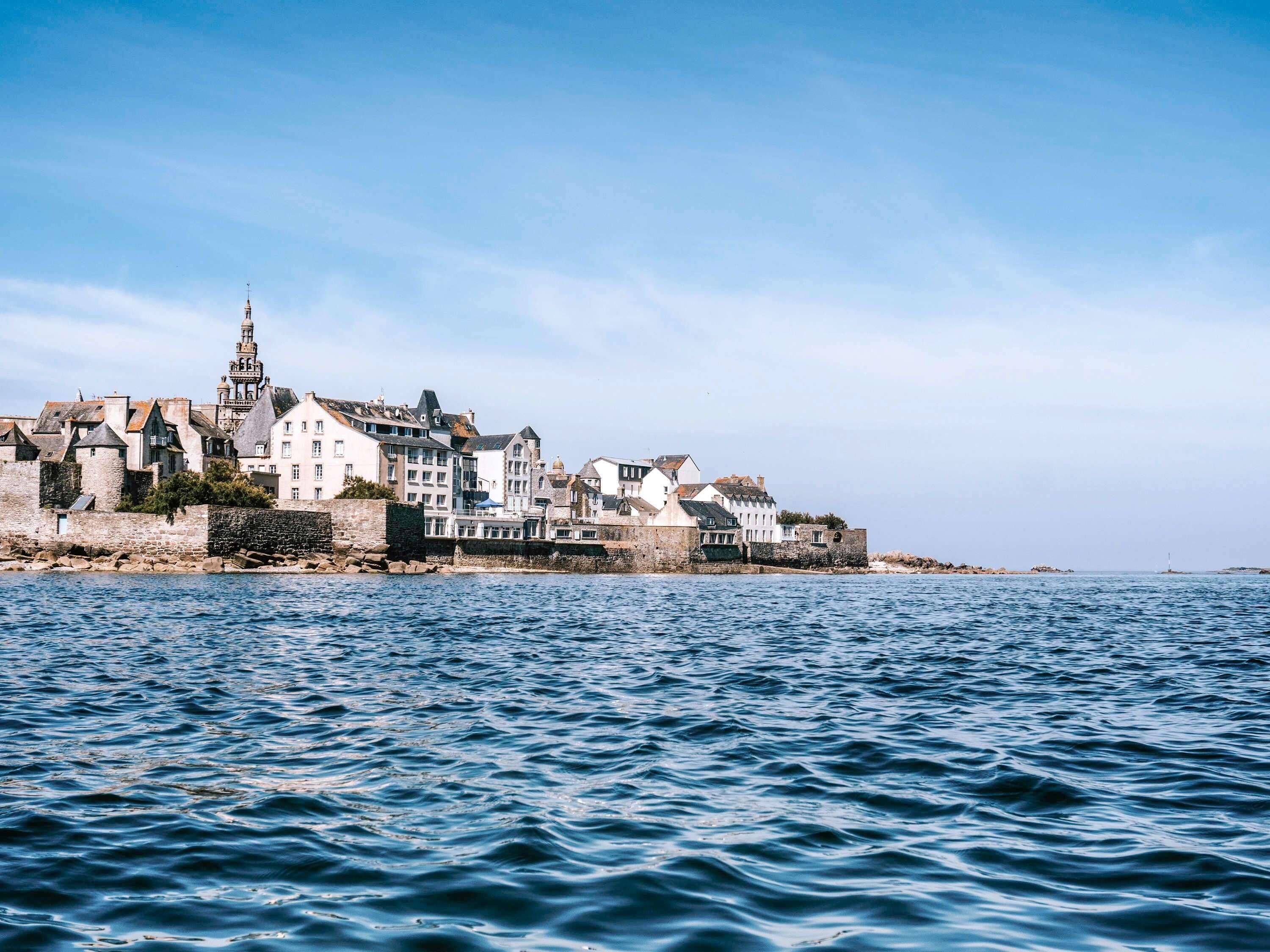 A coastal town with historic buildings, a prominent tower, and a stone wall along the waterfront.