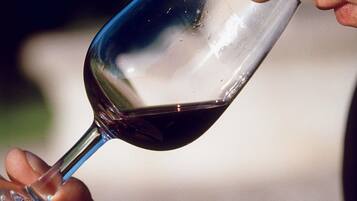 Una mano sosteniendo una copa de vino con un líquido oscuro, posiblemente vino, y un tallo transparente.
