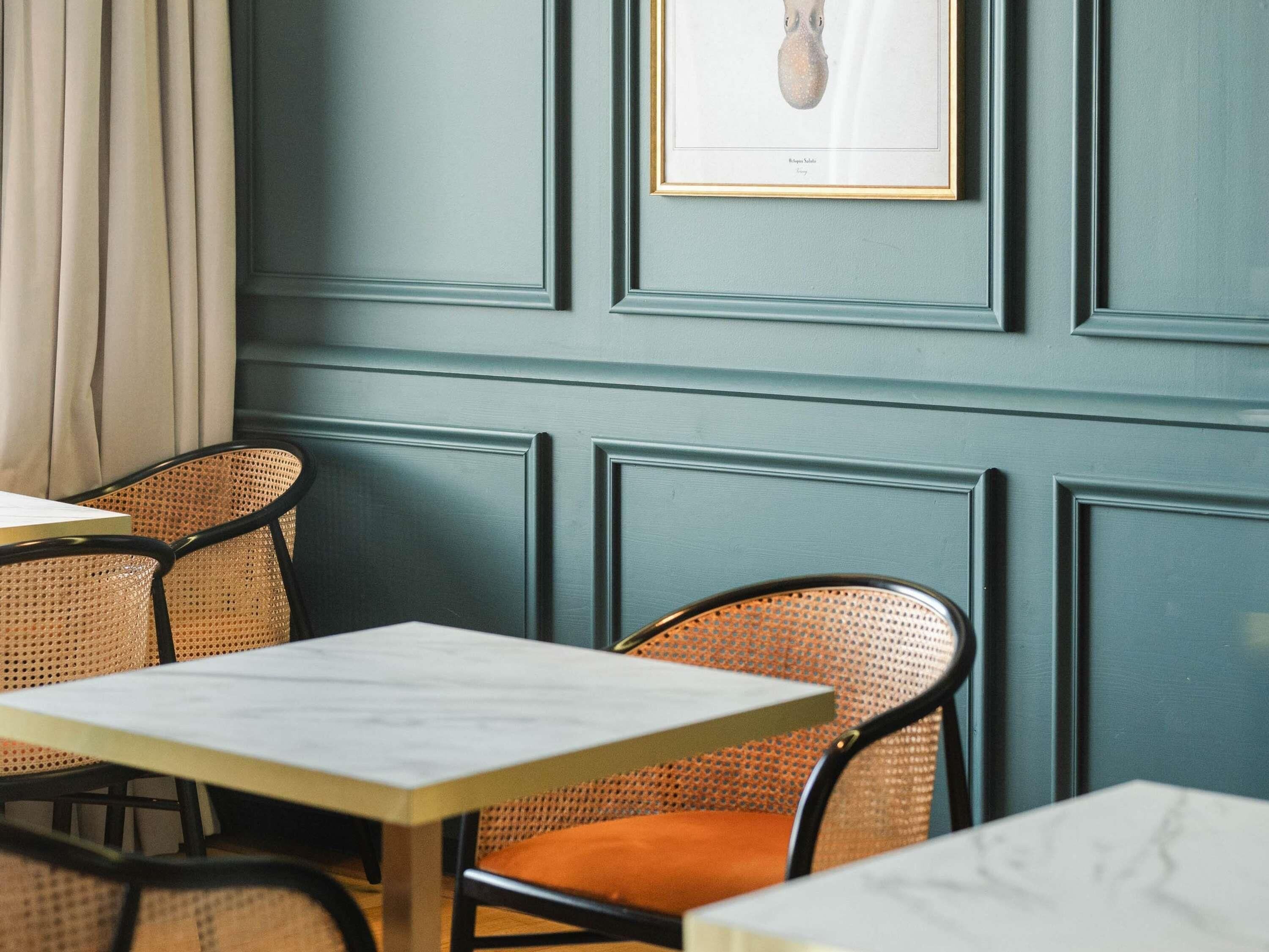 Un coin repas avec une table et des chaises, un tableau encadré au mur et une fenêtre avec des rideaux.