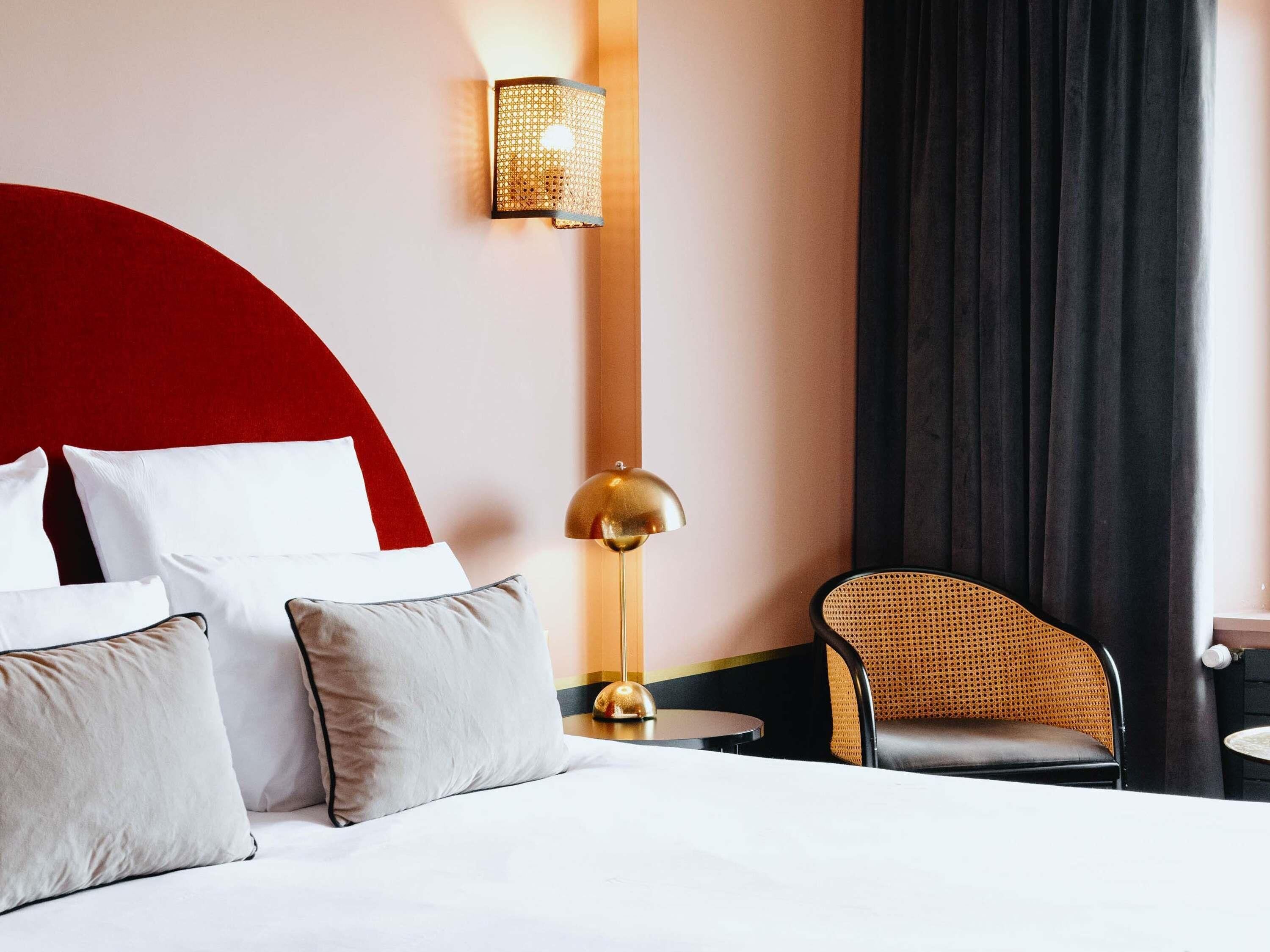 Une chambre d’hôtel avec un lit, une lampe, une chaise et un luminaire fixé au mur.