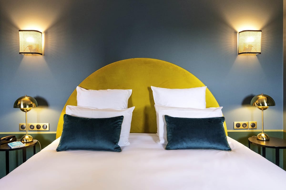 Een bed met een geel hoofdeinde, witte en donkerblauwe kussens, en twee nachtlampjes.