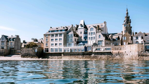 Un bâtiment situé au bord de l’eau, à étages multiples, doté de murs en pierre et d’une tour imposante.