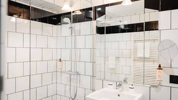 Un baño moderno con azulejos blancos, ducha con mampara de vidrio, lavamanos blanco y un espejo.