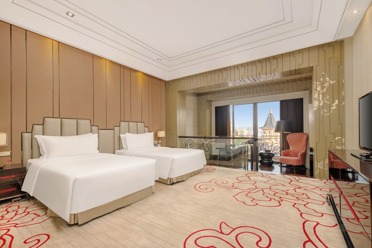 A hotel room with two beds, a balcony with a view, and a television.
