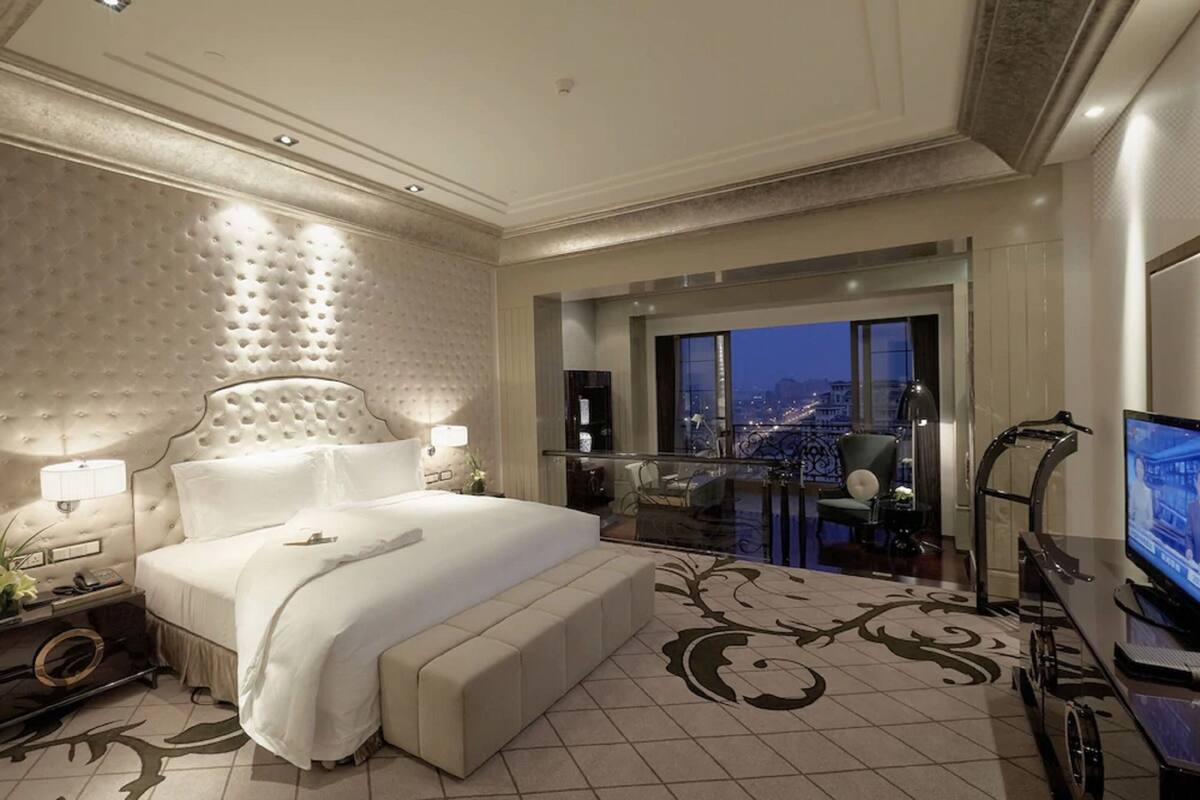Een ruime slaapkamer met een groot bed, een televisie en een balkon met uitzicht op de stad.