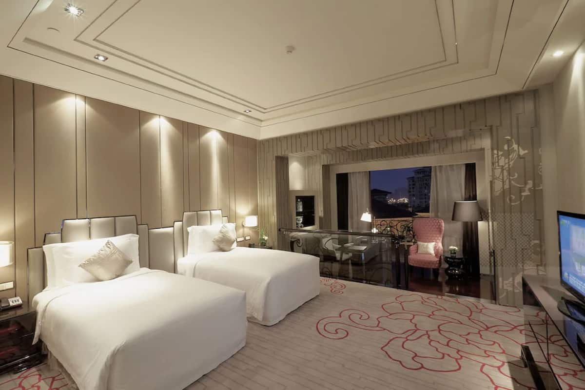 Een hotelkamer met twee bedden, een bureau, een stoel, een televisie en een balkon met uitzicht op de stad.
