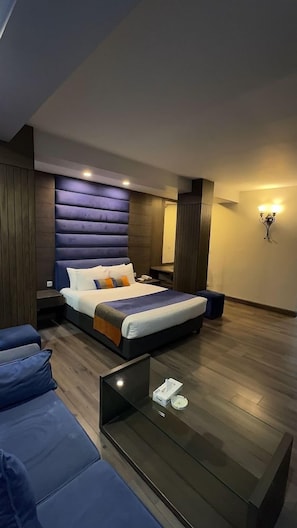 A modern bedroom with a large bed, a glass coffee table, and a blue sofa. - De Papae (Islamabad)