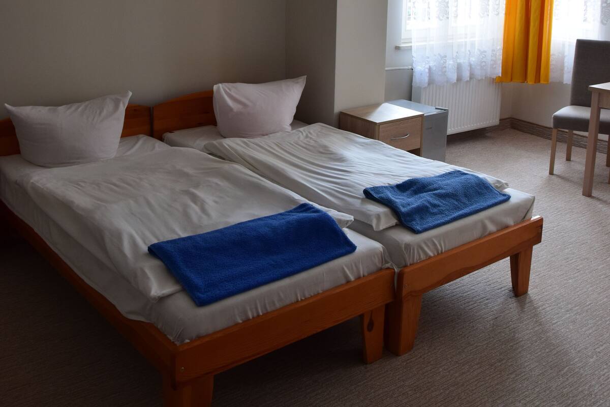Une chambre d’hôtel avec deux lits simples, un petit bureau, une chaise et une fenêtre avec des rideaux.