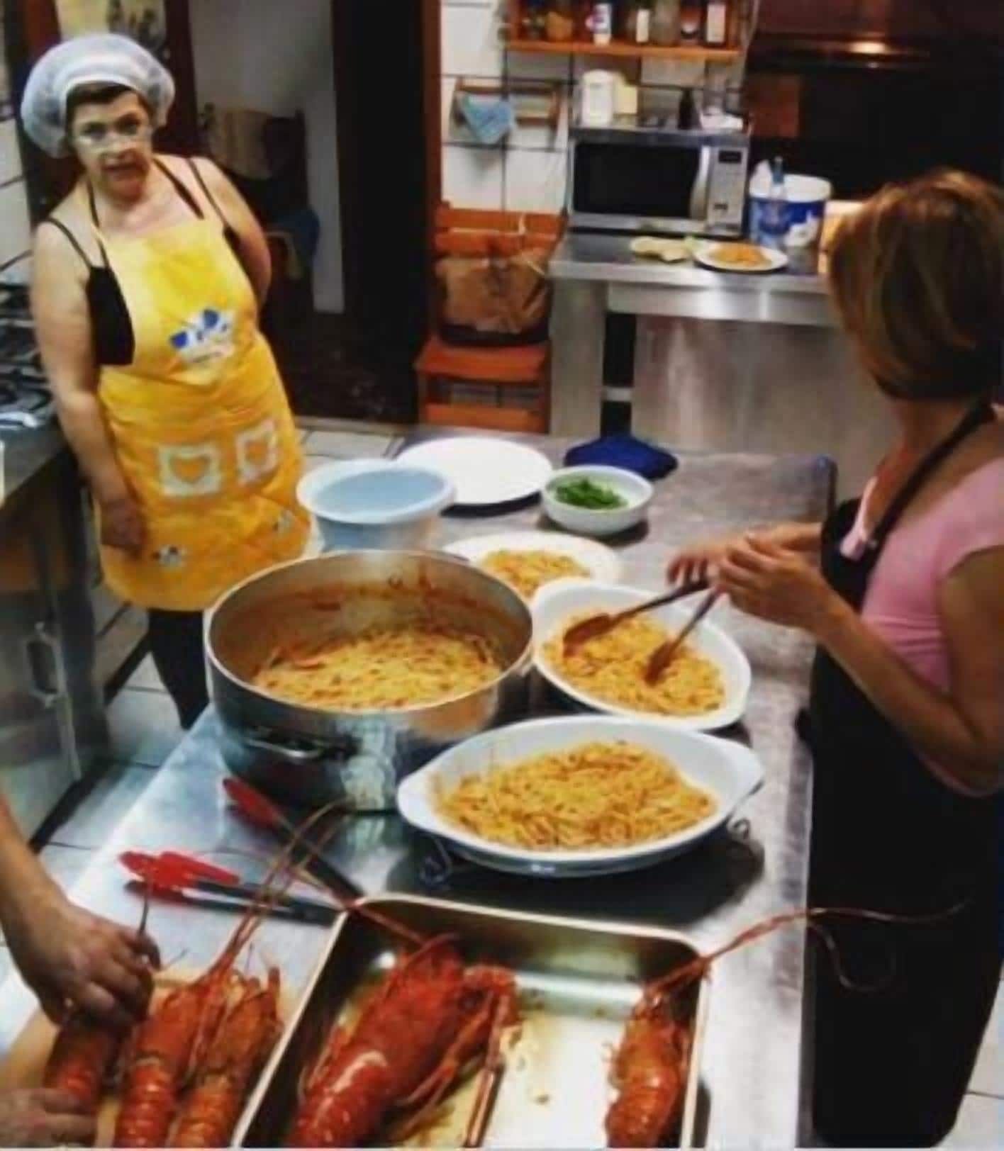 Une cuisine avec une grande marmite remplie de nourriture, plusieurs assiettes de plats et des homards sur un plateau.