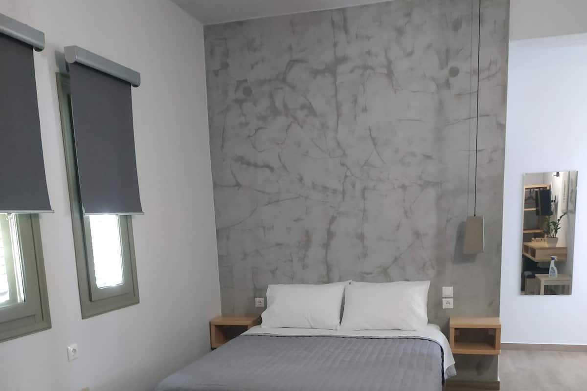 Et moderne soveværelse med seng, sofa, væg med marmorlignende mønster og en hængende lampe.