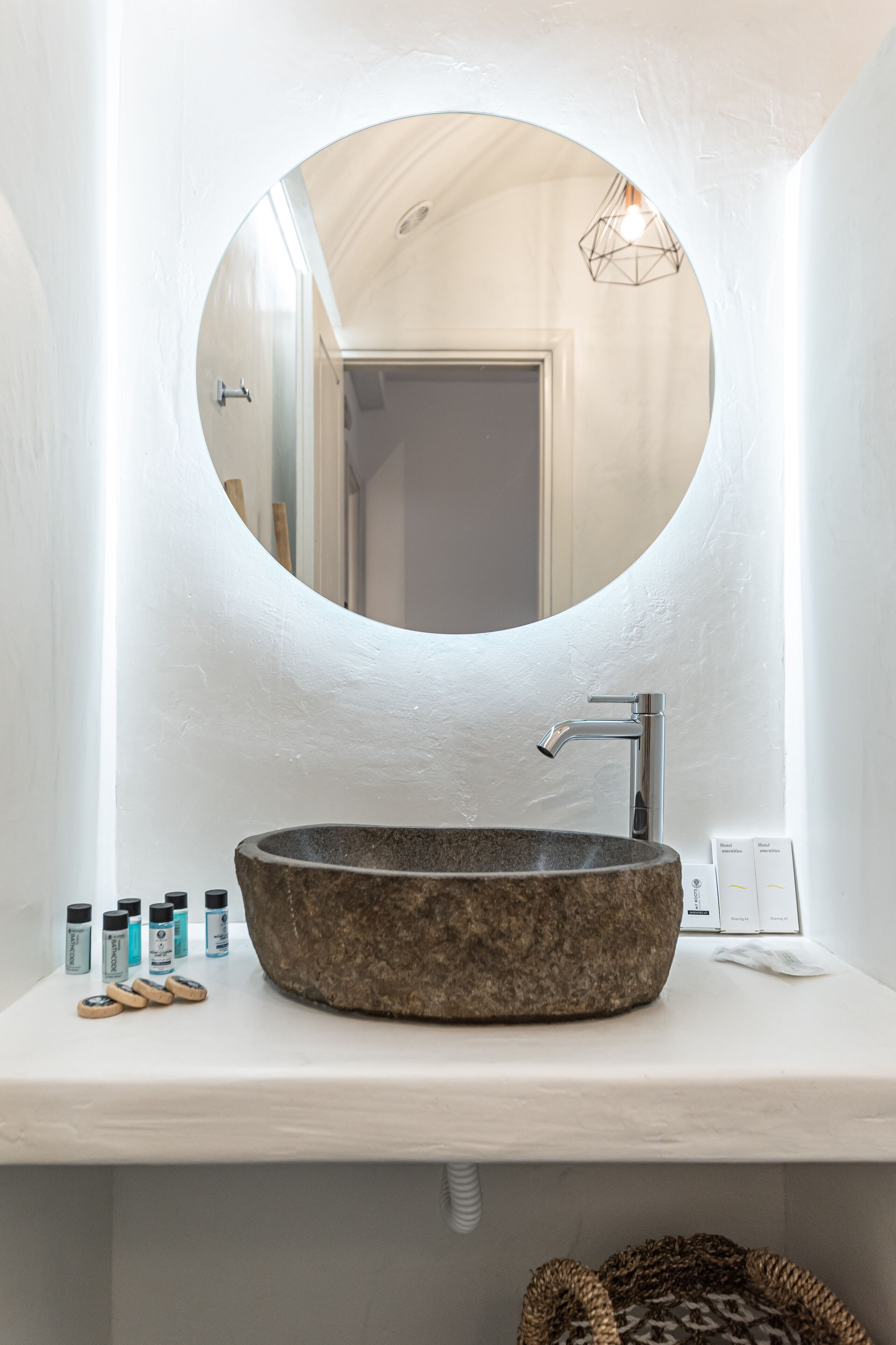 A bathroom with a round mirror, a stone sink, and a white countertop.